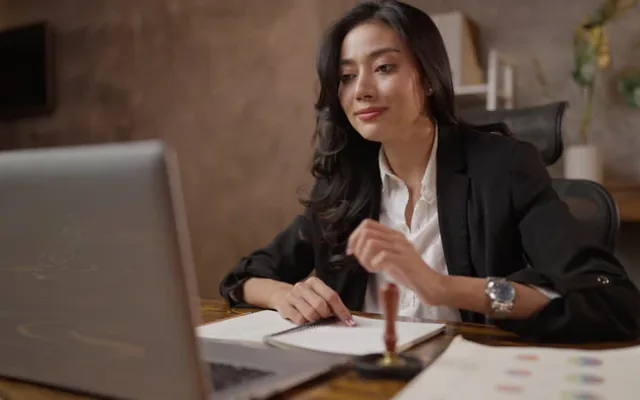Businesswoman working at a laptop with documents and a notebook